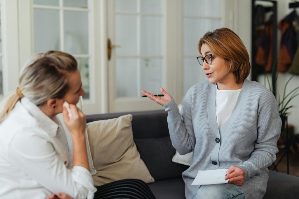 A counseling session with two women sitting on a sofa, engaged in conversation, indoors.